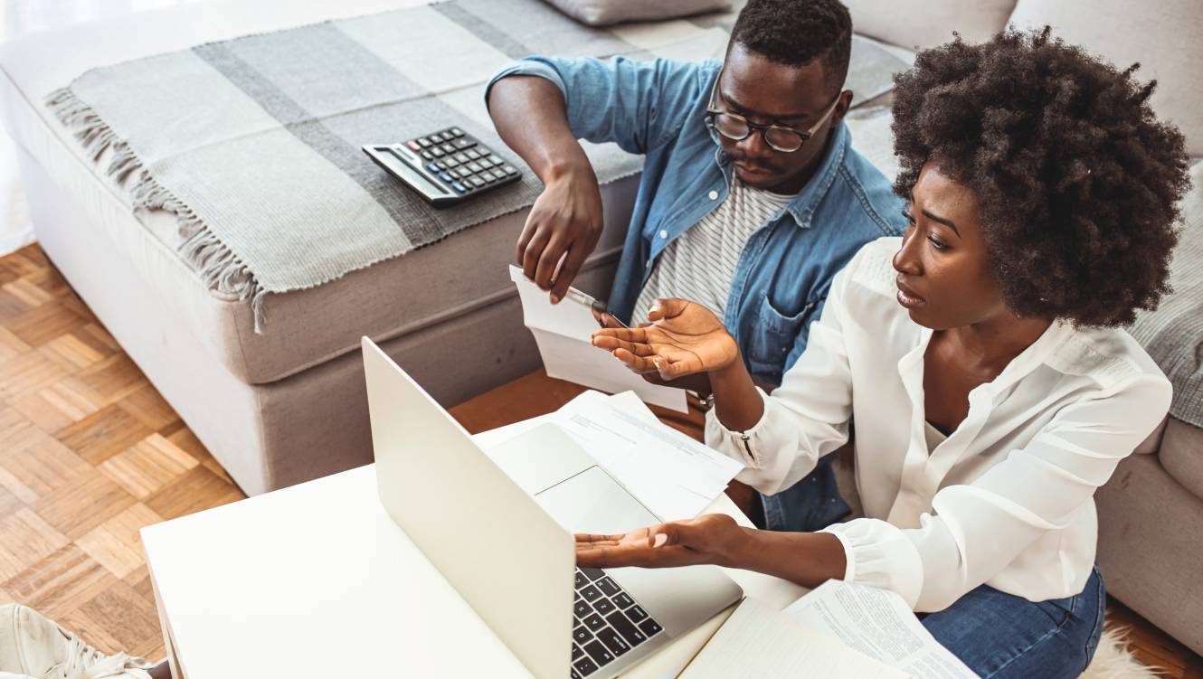 Serious African American couple discussing paper documents, sitting together on couch at home, man and woman checking bills
