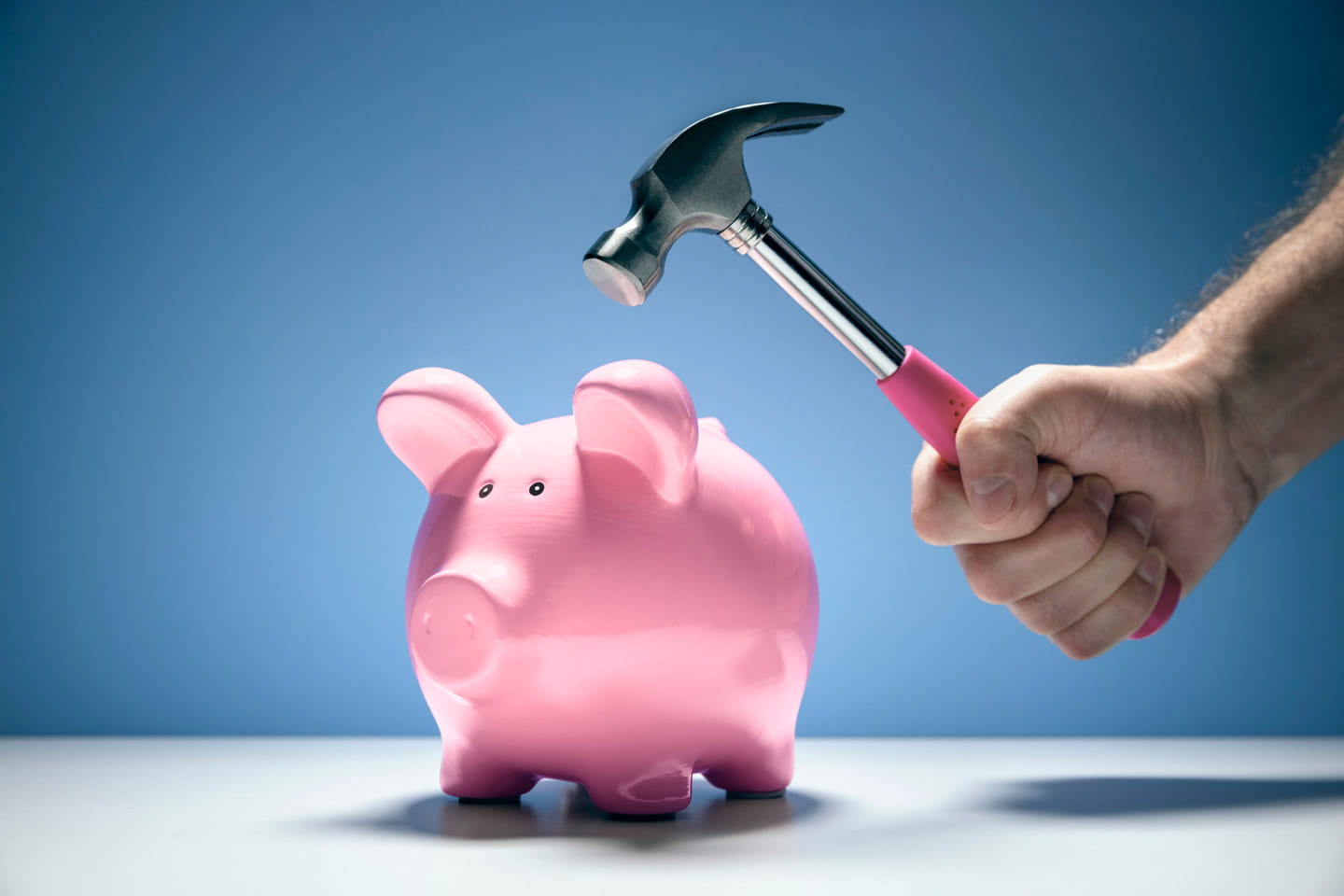 A pink ceramic piggy bank about to be struck with a hammer
