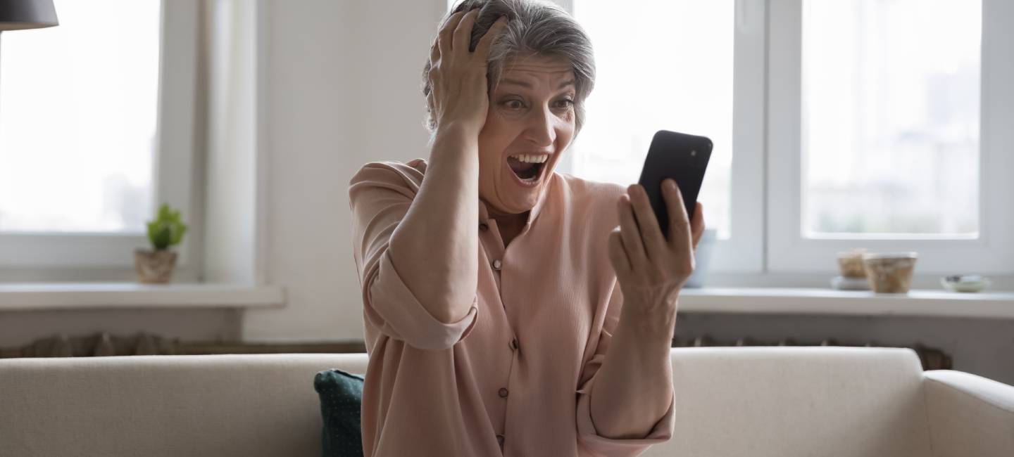 Excited happy mature mobile phone user woman shocked with good surprising news, looking at smartphone, reading notice, message on screen, holding head, shouting fro joy, rejoicing at success
