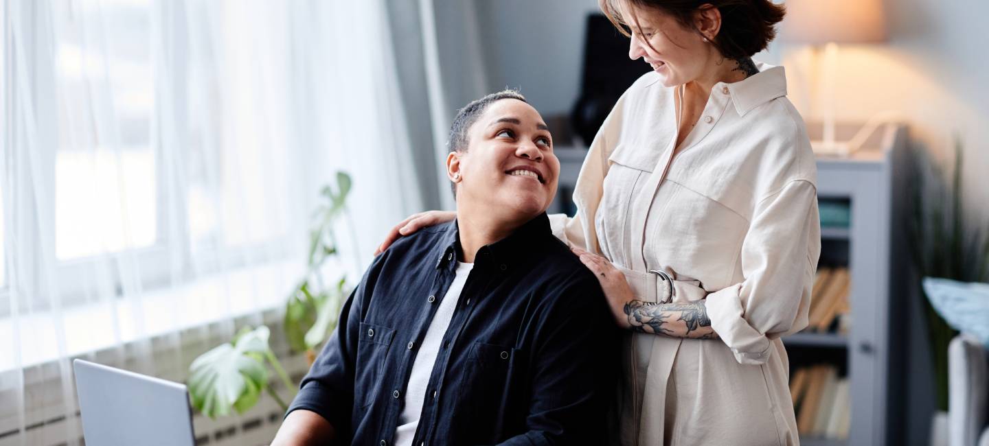 Portrait of two women using laptop at home together, one looking up towards the other