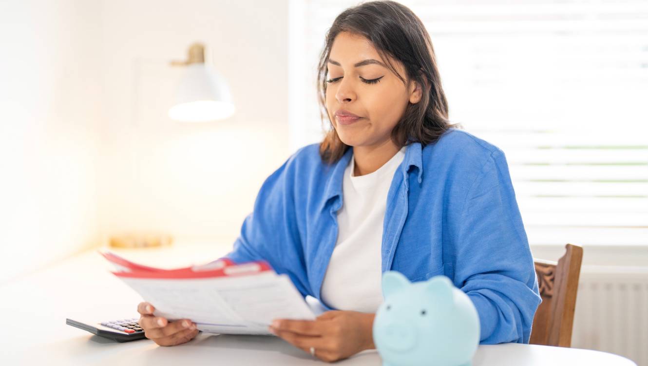 Woman reviewing financial documents at home with a piggy bank and calculator on a sunny da
