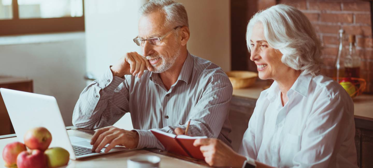 Positive mature couple sitting in the kitchen, on the laptop plaining finances 