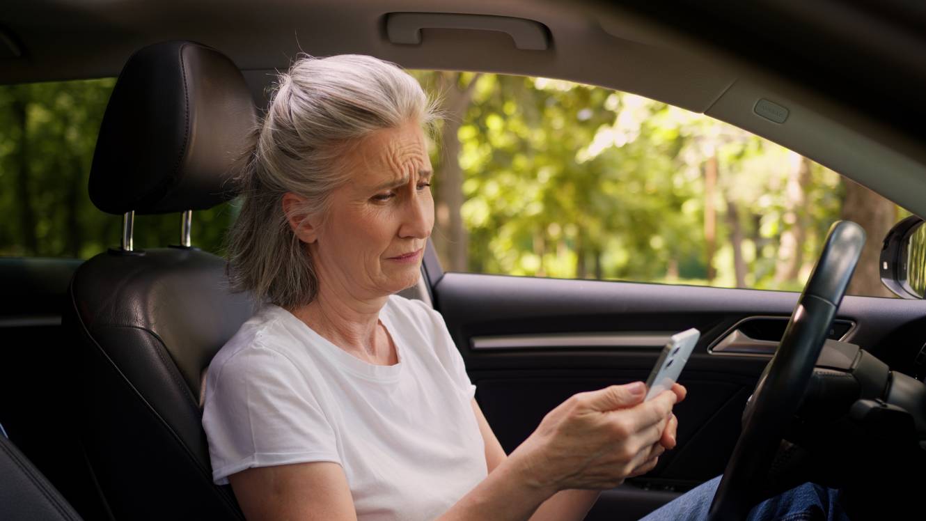 Woman sitting in her car looking at her phone looking concerned