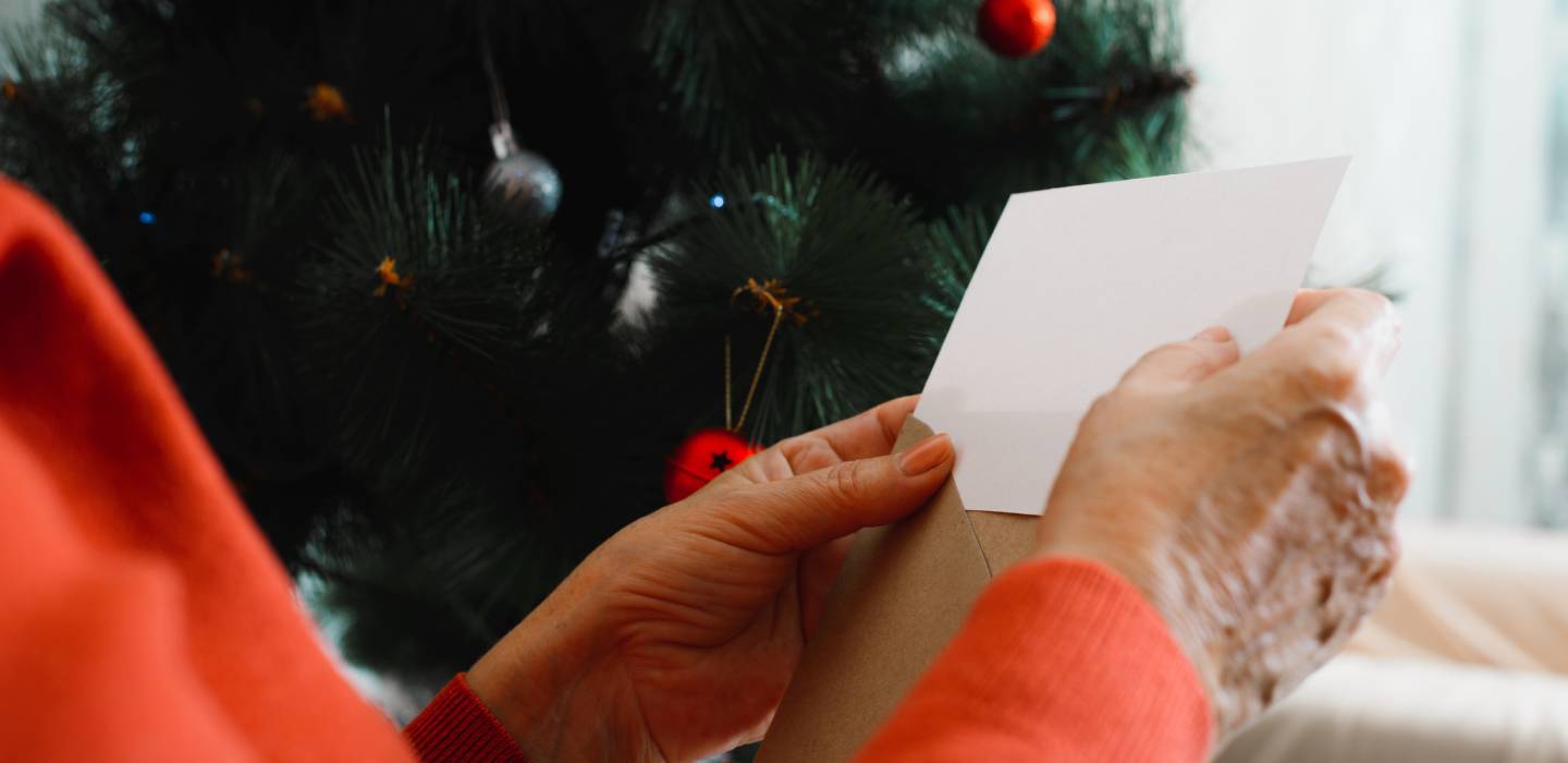 Side view of senior woman's hand holding blank white greeting card against of Christmas tree.