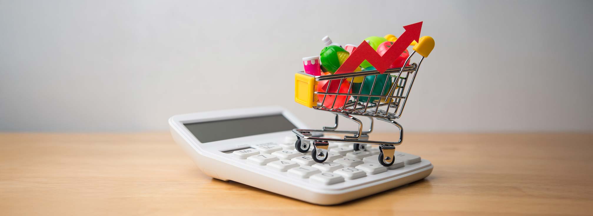 Vegetables, fruits, drinks, food material in supermarket trolley and calculator on wooden table. Rising cost of living, food price increase, inflation crisis, home finance and spending money concept.
