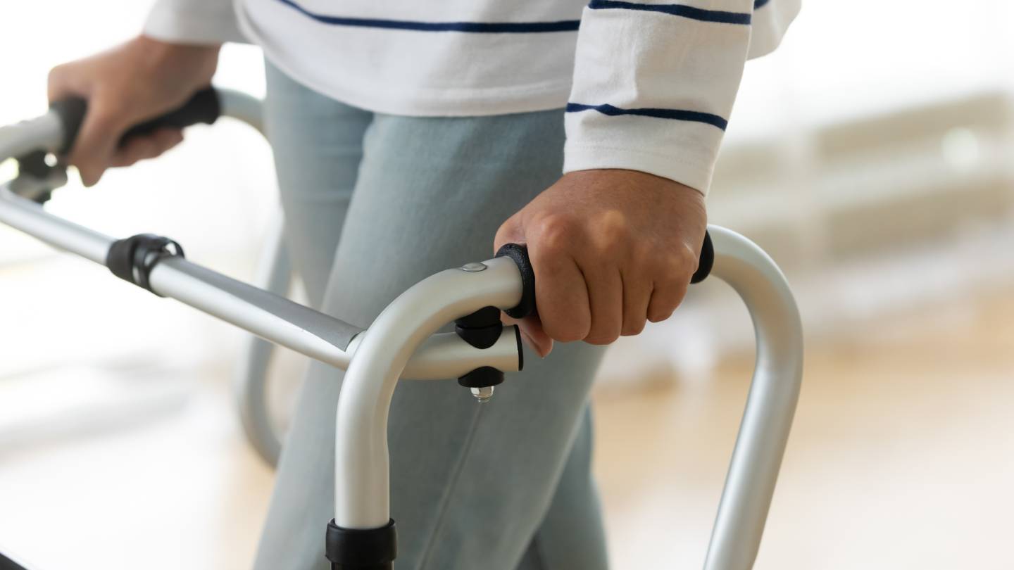 Disabled senior woman standing alone holding walking frame at a care home