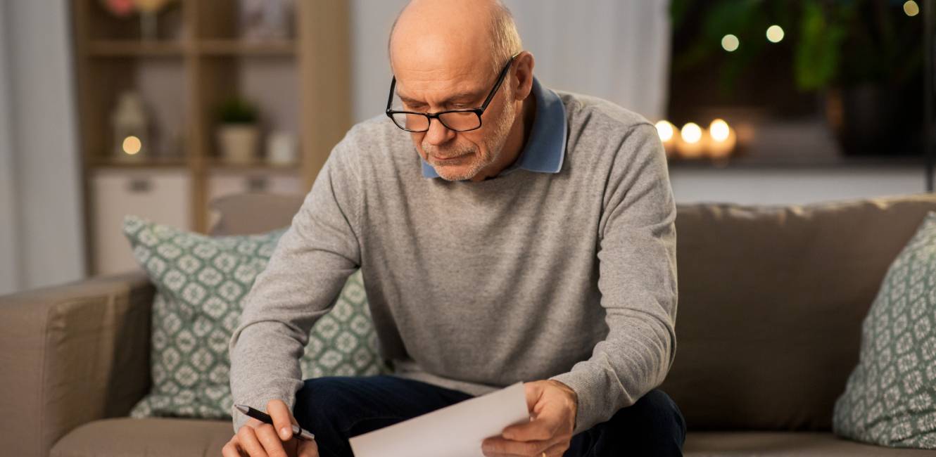 savings, annuity insurance and people concept - senior man with papers or bills counting on calculator at home in evening