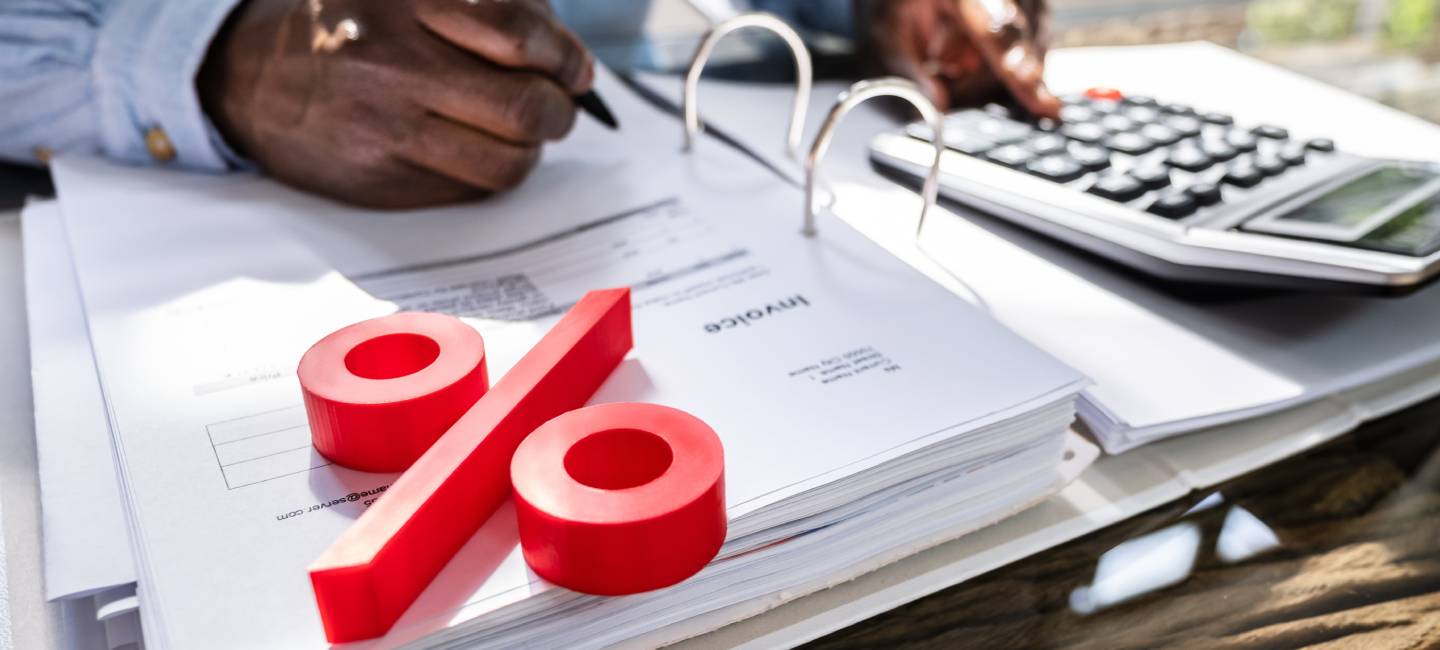 A person holding a pen calculating interest rates with a red percentage on his paper and a calculator 