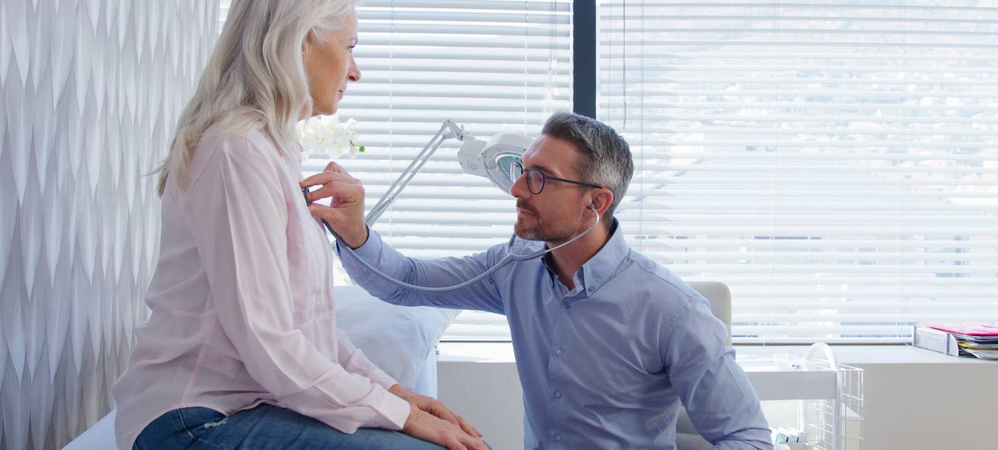 Doctor listening to mature female patient breathing with stethoscope during medical exam