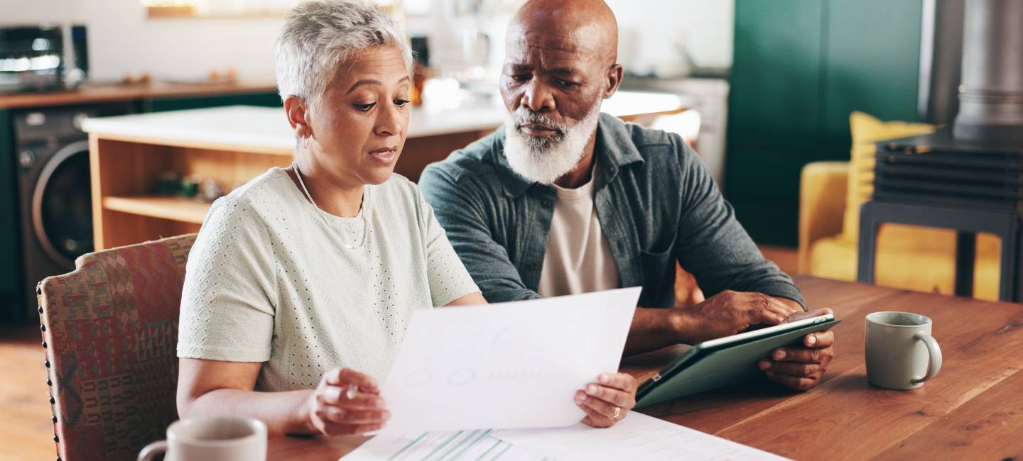 Mature couple reviewing documents with tablet for financial discussion, planning or expenses at home. 