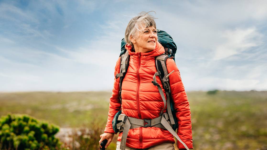 A mature woman in hiking gear looks smilingly to the right in a field 