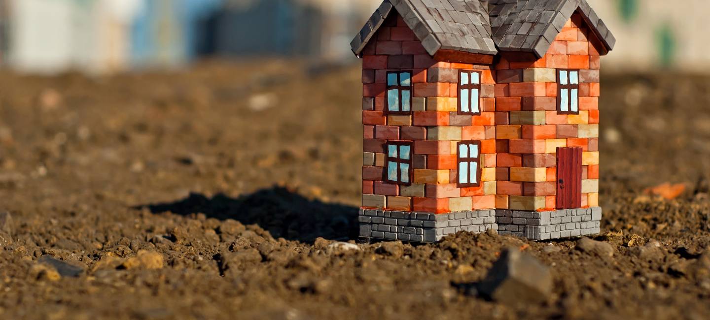 Brick toy house on the ground. Orange house on brown earth. 
