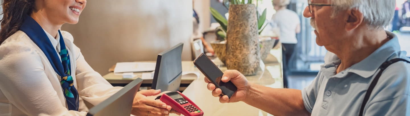 A senior man is paying for a hotel stay using a contactless payment method