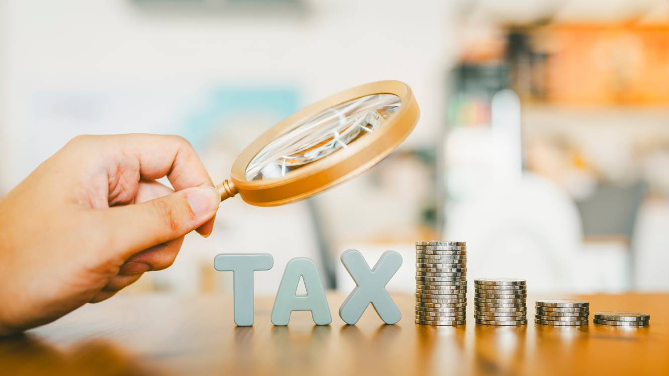 Hand holding magnifying glass looking at tax letter and money coin, stack of money rising up, concept of tax payment and tax deduction.