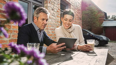A mature couple are looking intently at a tablet computer as they drink coffee at a courtyard table