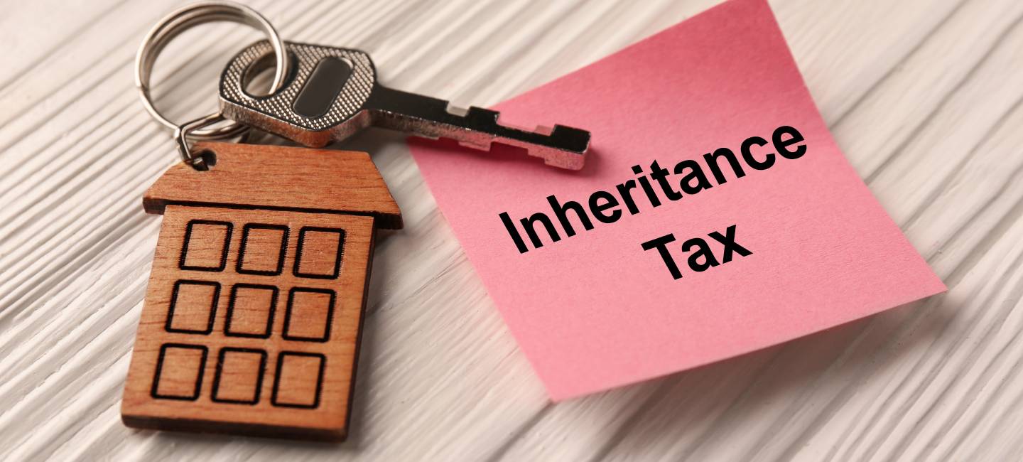 Inheritance Tax. Paper note and key with key chain in shape of house on white wooden table, closeup