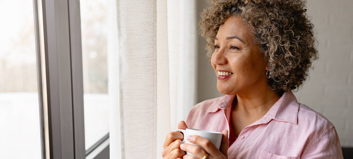A woman holding a tea cup, looking smiling out the window