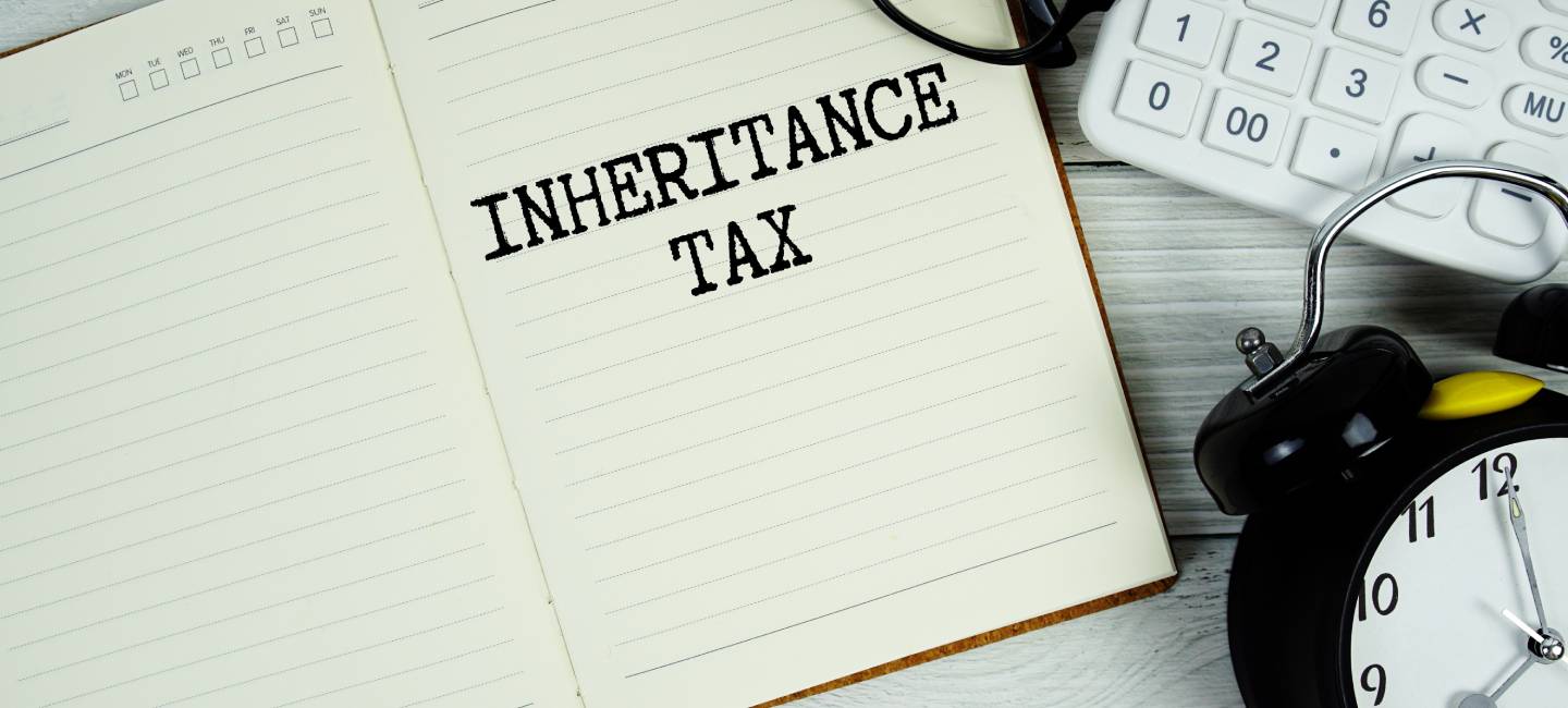 Inheritance Tax text on notepad with alarm clock, eyeglasses and calculator on wooden background