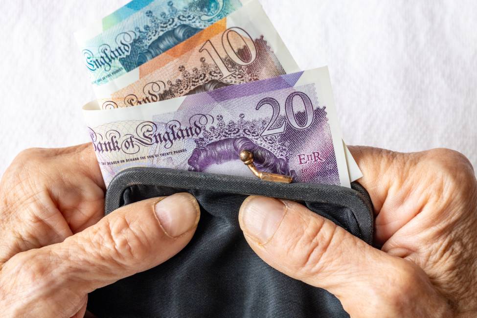 An older lady holds an old fashioned purse with British pounds in her hands.