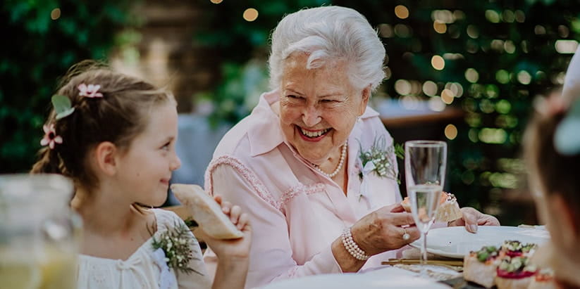 Grandmother sharing a joke with a young bridesmaid at a summer wedding.