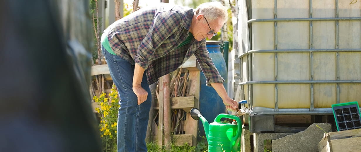 Senior man collecting water from the rainwater tank in the garden.