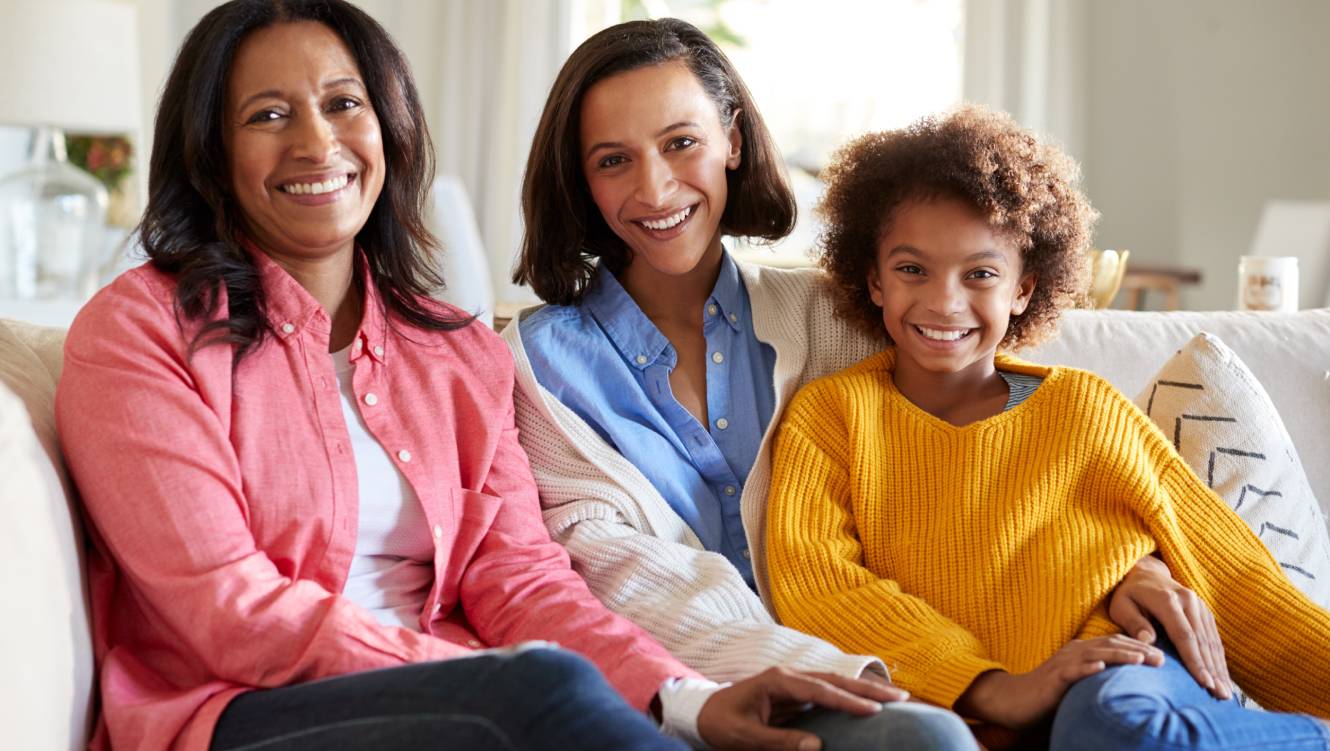 Three generation African American family female family group sitting on a sofa in the living room smiling to camera,