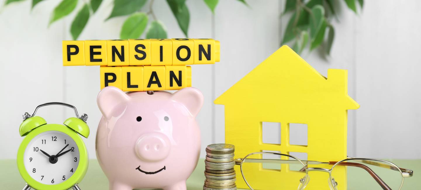 Yellow cubes with phrase Pension Plan, piggy bank, stack of coins and alarm clock on light green table. Retirement concept