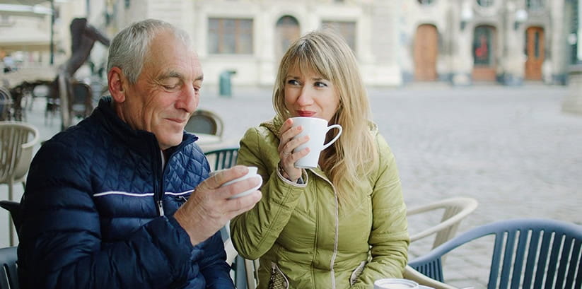 Happy couple with age difference drinking coffee in cafe with terrace outdoors in the morning during early autumn