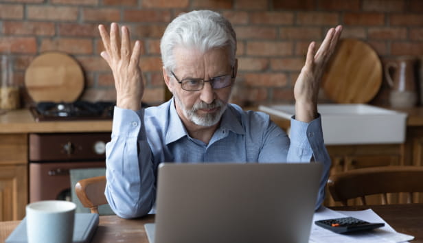 A man sat in front of a laptop with his hands held up in frustration