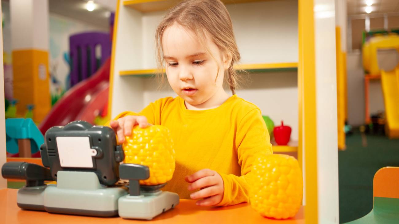 A little girl in a yellow sweater playing with a toy cash register 