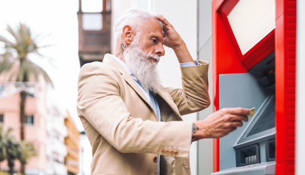 A man at a cash machine holding his head