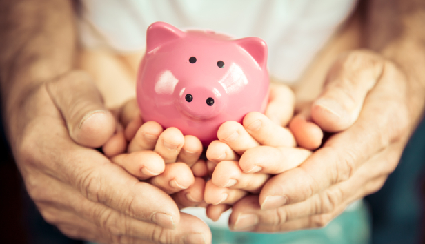 Adult hands cupping a child's hands holding a piggy bank