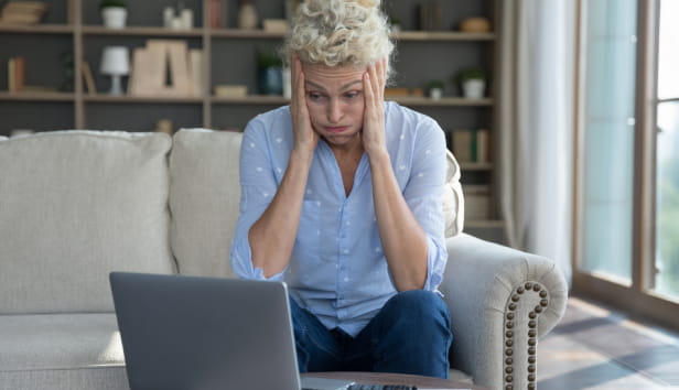 A distressed woman looking at her laptop with her head in her hands