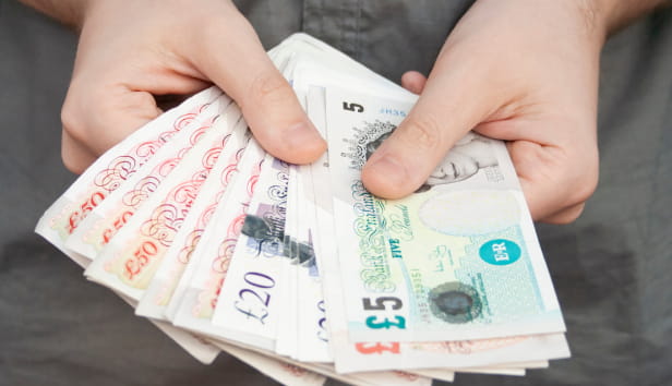 A person holding several £5, £10 and £20 notes