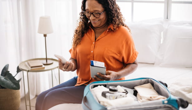 A woman holding her phone, passport and boarding pass next to an open suitcase