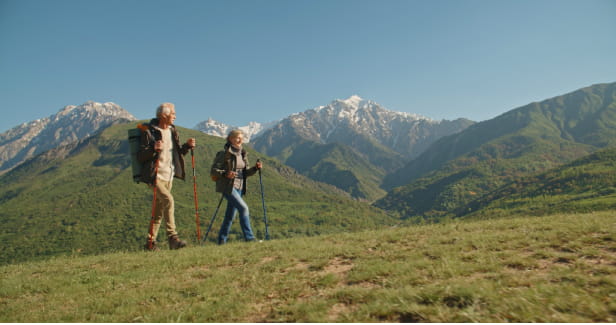 A couple hiking with walking sticks. In the background are some glorious mountains. 
