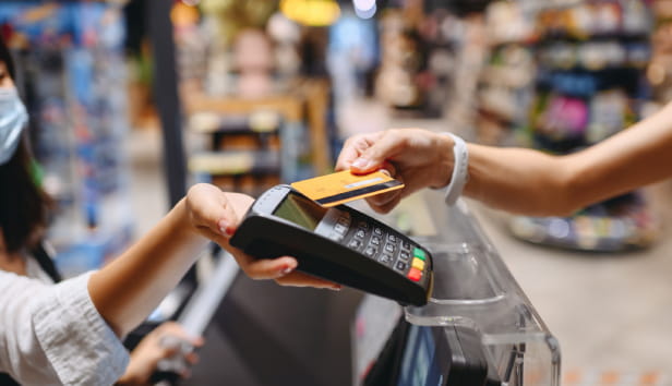 A shopkeeper is holding out a card reader and another person is tapping their card on the card reader