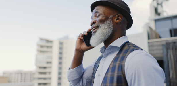 A man with a hat and beard talking outdoors, laughing and chatting on his mobile phone