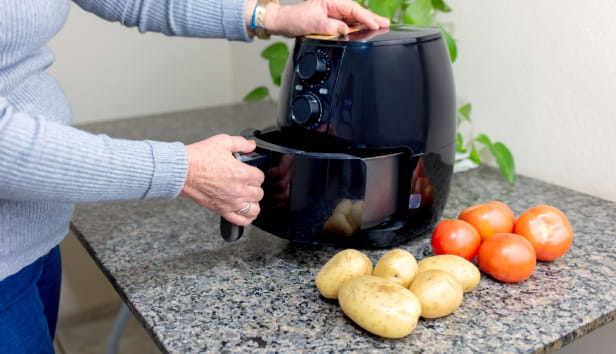 Using airfryer to fry food in home kitchen, with tomatoes and potatoes nearby