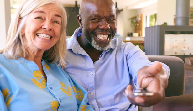 Multi-Racial Senior Couple On Sofa At Home Together Watching TV.