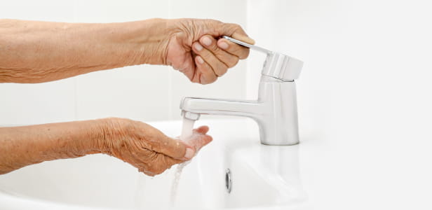 Elderly woman washes hand in bathroom