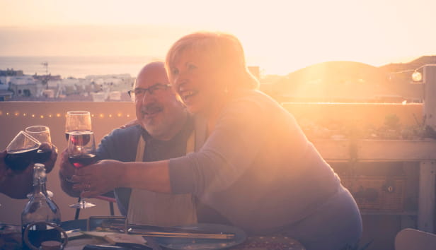 group of aged senior friends adults having dinner and doing party nice time in the rooftop terrace outdoor with wine and food. having fun during the sunset with beautiful sun backlight and amazing vie