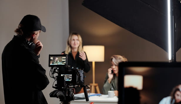 Back view of young videographer standing in front of steadicam during shooting of commercial with female model in studio