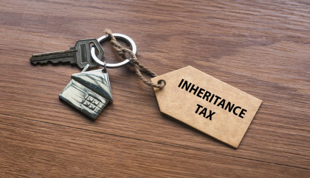 A house key with a tag written with Inheritance Tax on wooden background.