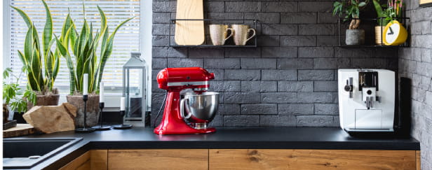 Wooden clock on black brick wall in trendy kitchen with red kitchen robot.