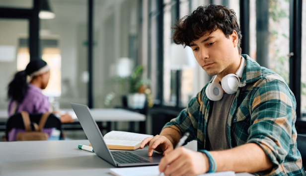 University student writing while using laptop and studying in the classroom. Copy space.