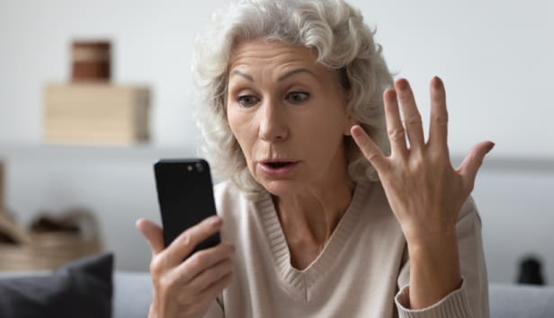 Angry shocked mature phone user staring at screen in surprise. Elderly lady worried about app error, data stealing, scam, bad news, problems with smartphone. Annoyed woman using cell for video call.