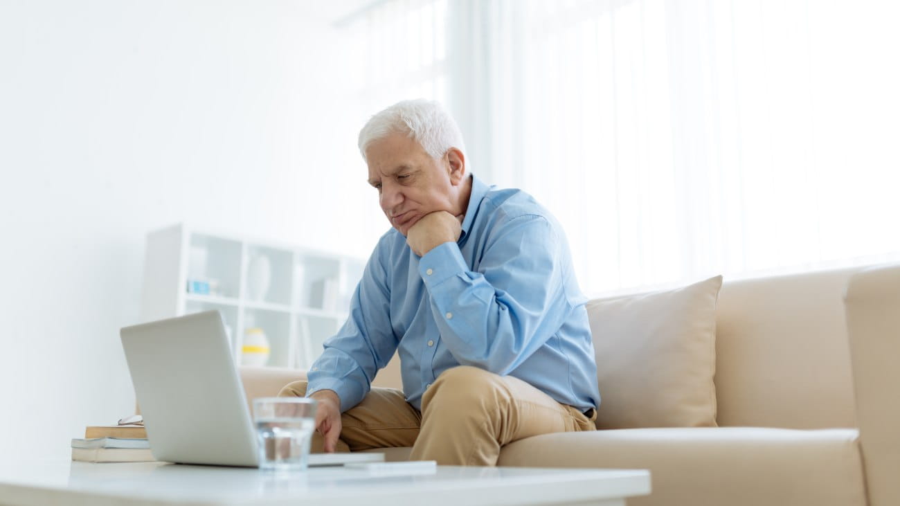 A man sat on the sofa, with his head resting on his fist, looking at an open laptop