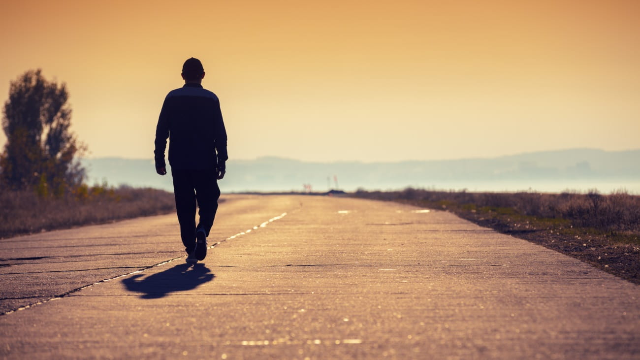 A person walking along an open road in to the sunset