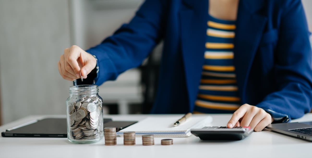 A person using a calculator and also adding coins to a jar